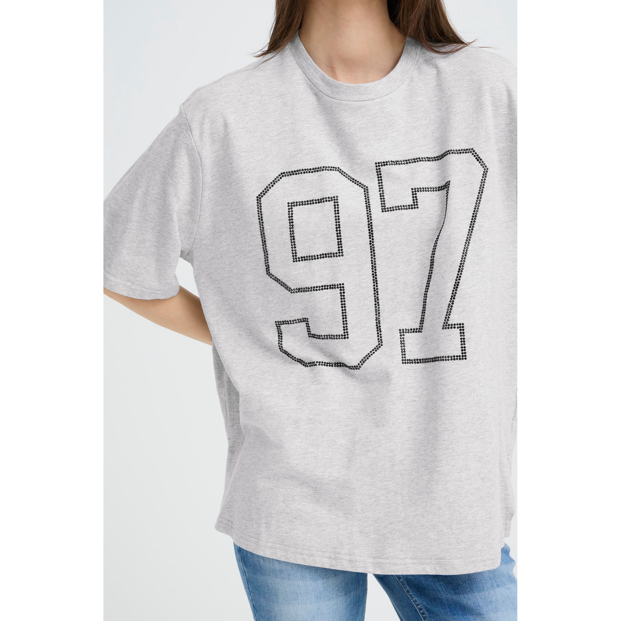 Model i grå t-shirt med 97-tal i sorte sten og jeans, tæt på forfra