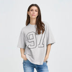 Model med hænderne i lommerne i løs grå t-shirt fra Pulz med 97-motiv