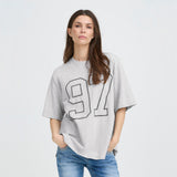 Model med hænderne i lommerne i løs grå t-shirt fra Pulz med 97-motiv
