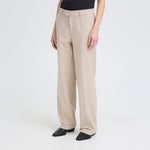 Model i beige wide leg bukser med høj talje, stylet med sort top og sorte støvletter, set skråt forfra