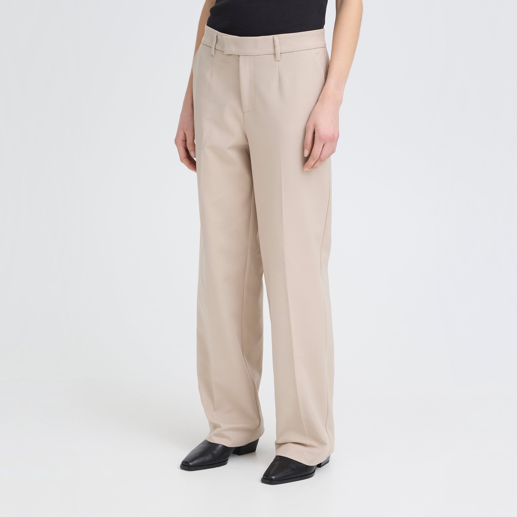 Model i beige wide leg bukser med høj talje, stylet med sort top og sorte støvletter, set skråt forfra
