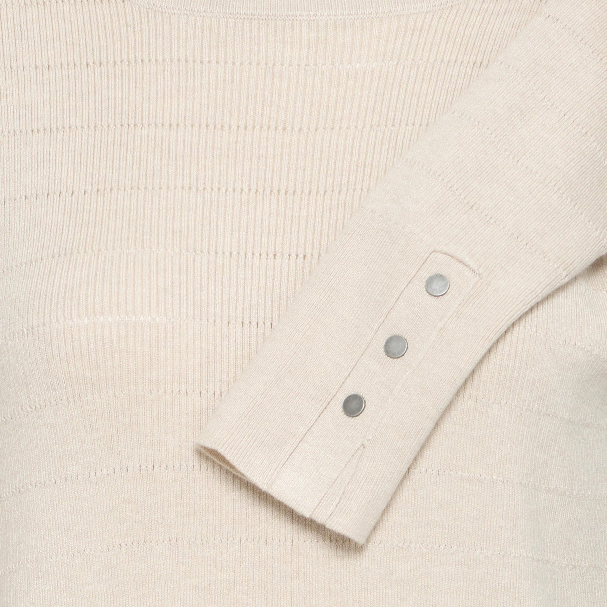 Nærbillede af beige pullover i ribstrik med hulstriber og tre sølvfarvede knapper ved ærmet