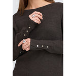 Model i brun pullover, tæt på bådudskæringen og de sølvfarvede knapper ved ærmerne