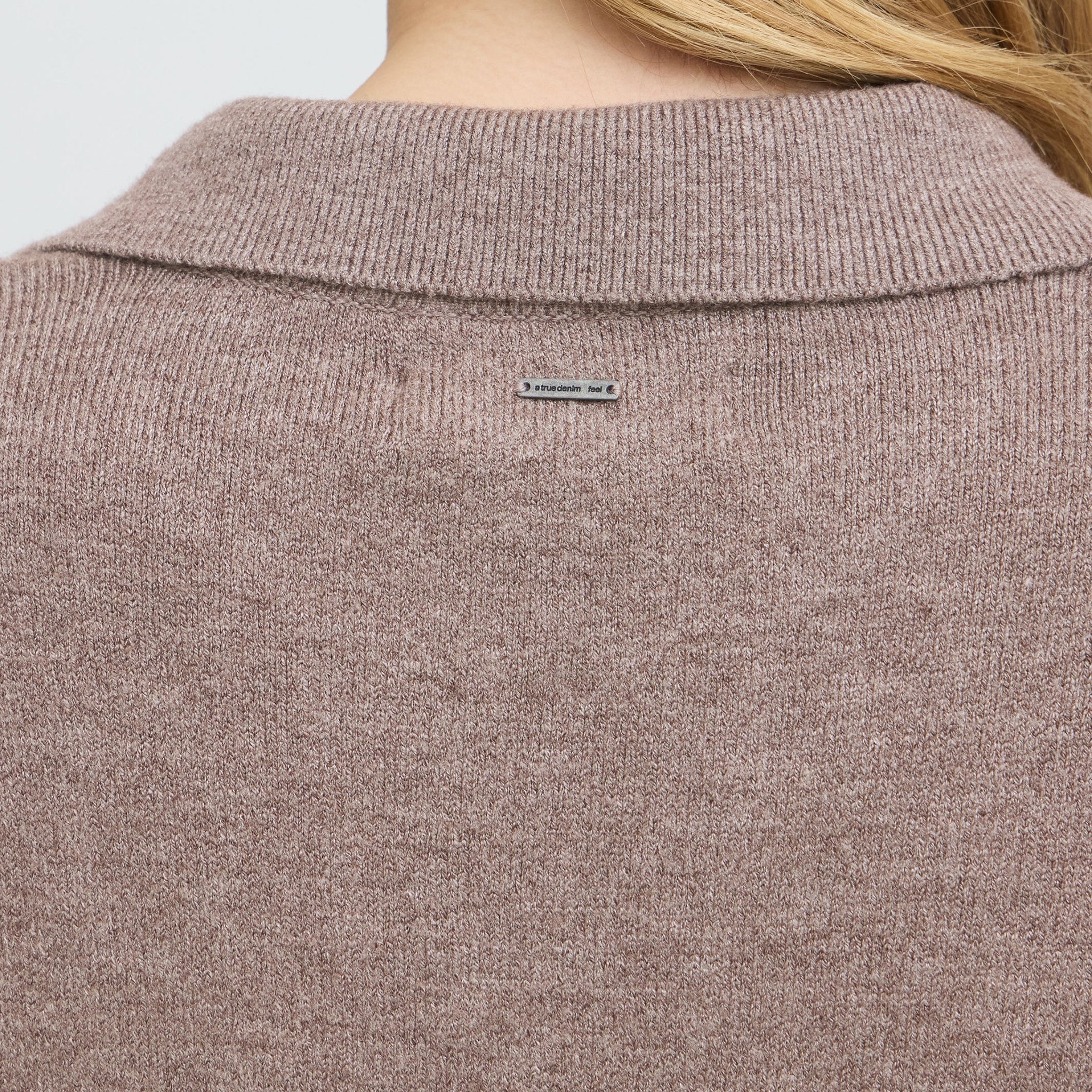 Detalje bagfra af brun pullover med ribbet krave og logoskilt i metal