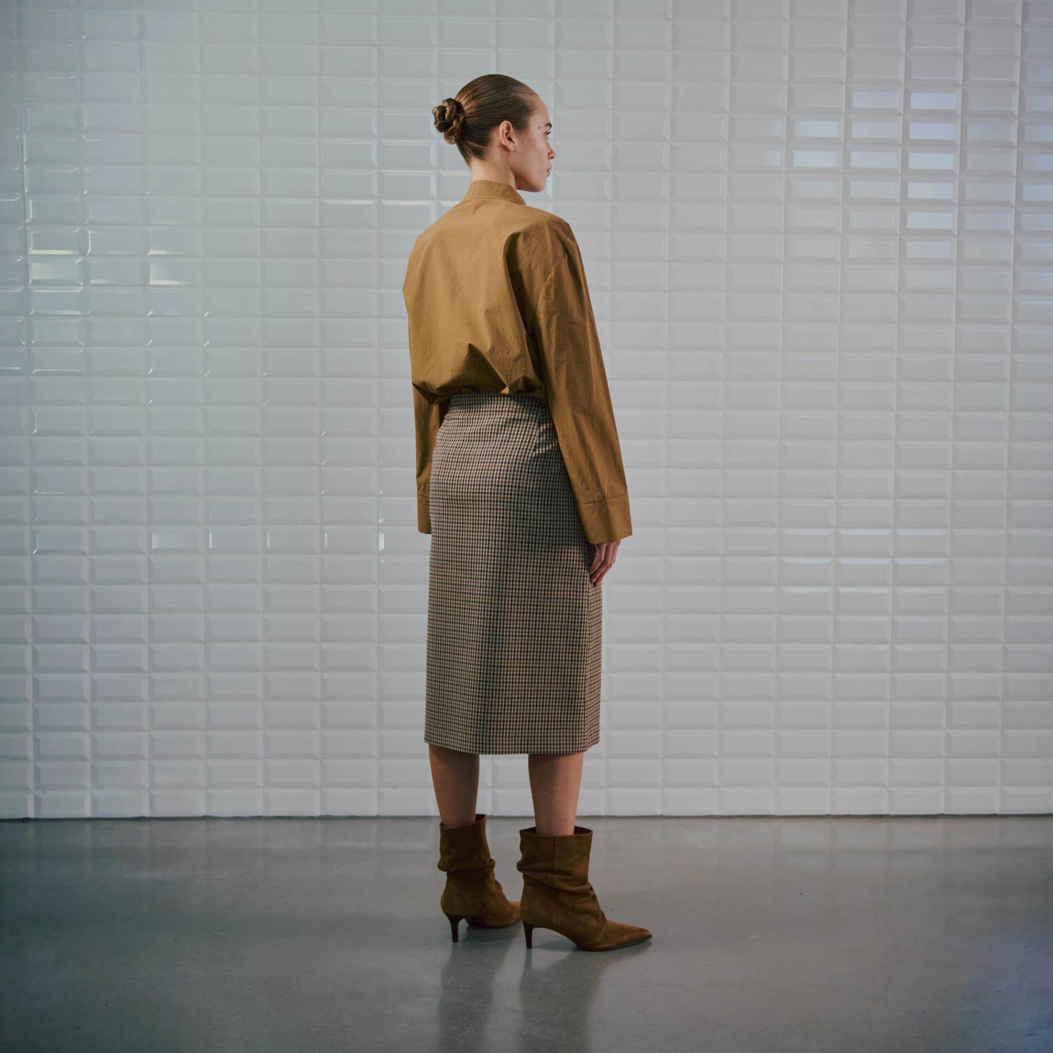 Model i brun og beige ternet midi nederdel set bagfra, stylet med brun skjorte og støvler
