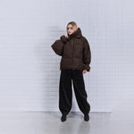 Model i brun puffet jakke fra WithBlack med høj krave og hætte, stylet med mørke bukser og støvler