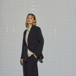Model i navy blazer med nålestriber over en beige skjorte, set skråt forfra