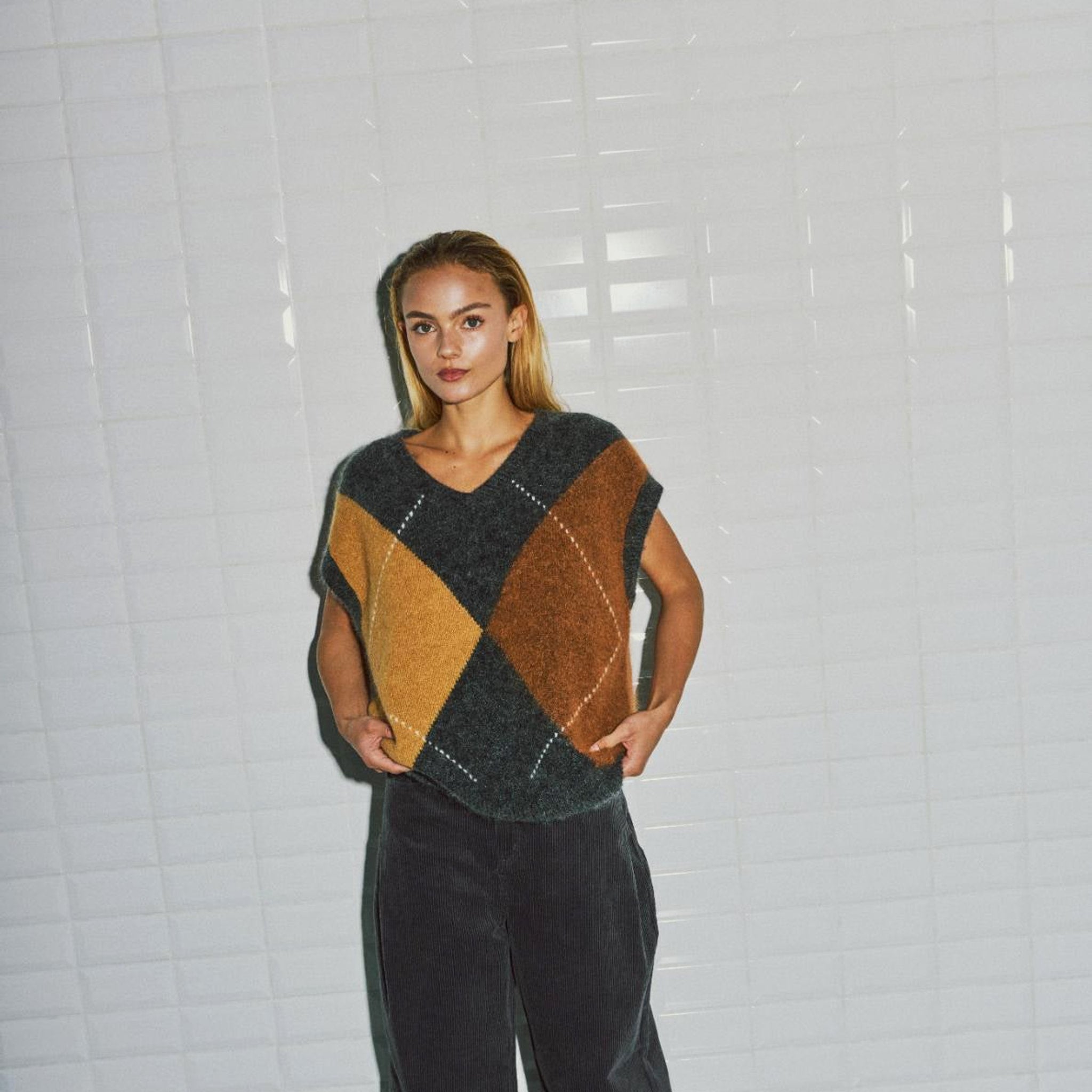 Model i beige harlekin vest med V-udskæring fra WithBlack, set forfra med vide mørke bukser
