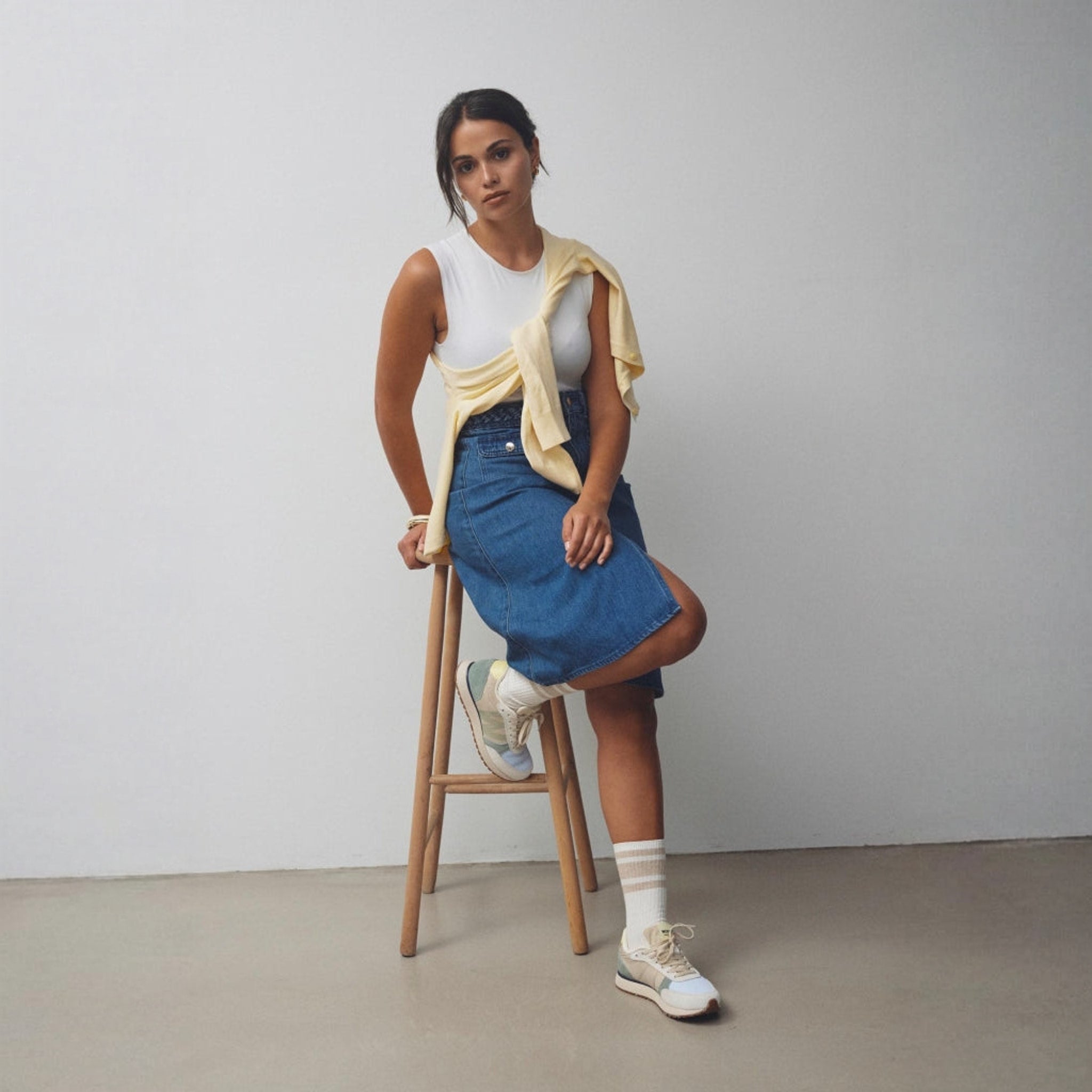 Model sidder på skammel i flerfarvede Woden Ronja sneakers og nederdel i denim