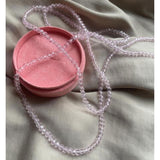 Pink halskæde med små facetterede, gennemsigtige perler fra Wolff Jewelry liggende på lyst stof