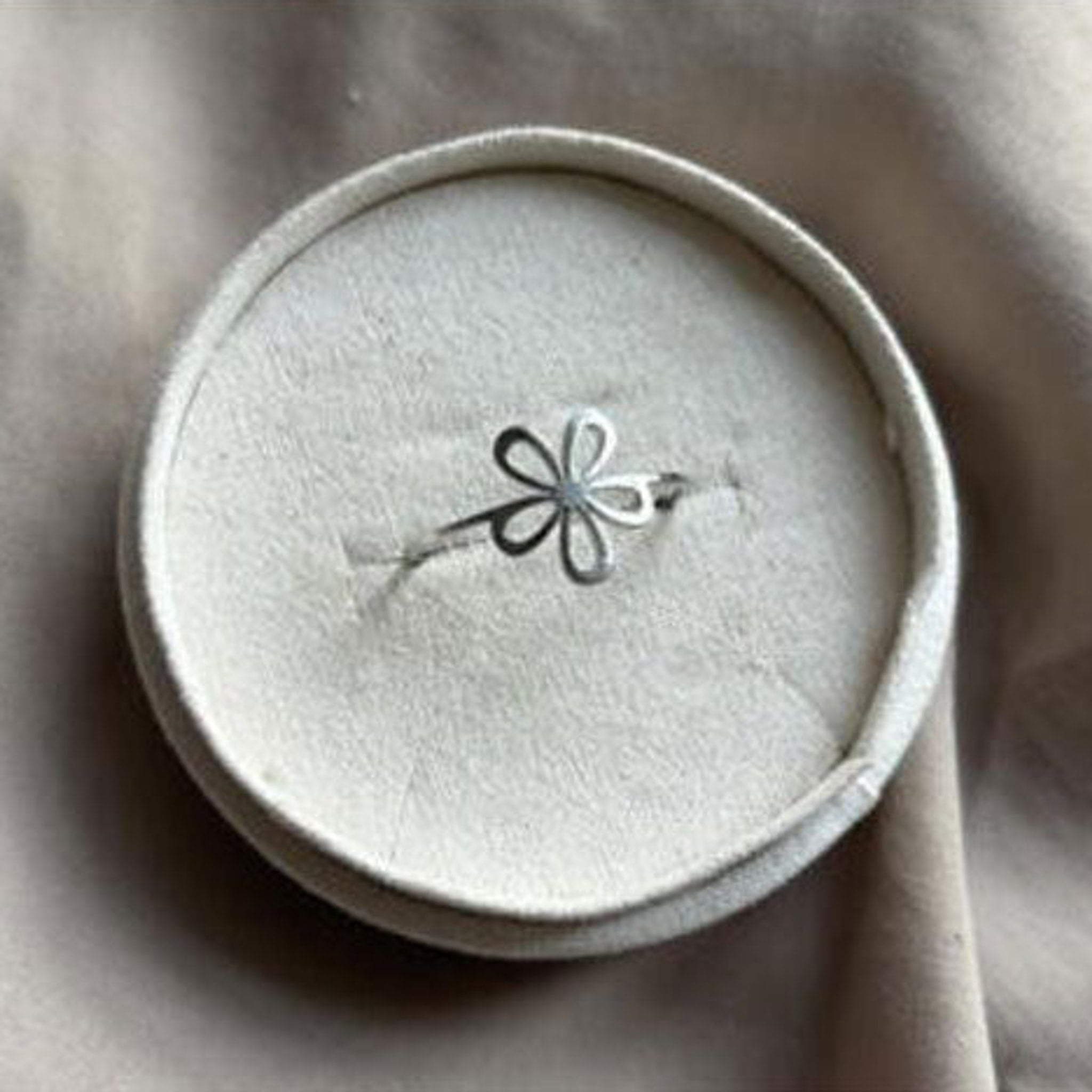 Sølvfarvet Chipsy ring fra Wolff Jewelry med åben blomst og tyndt bånd i en rund beige smykkeæske