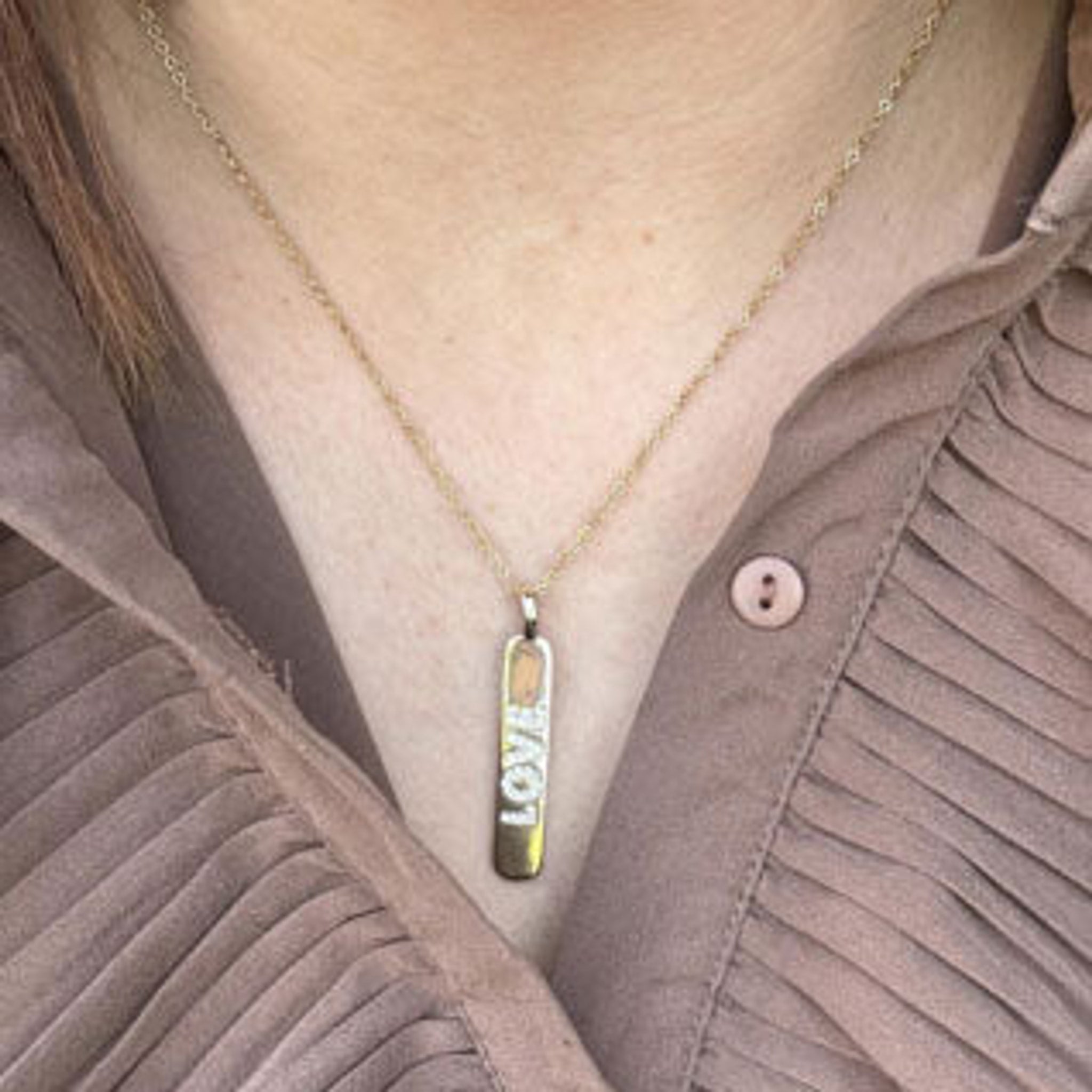 Halskæde fra Wolff Jewelry med aflangt LOVE-vedhæng båret over en brun plisseret skjorte