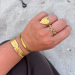 Guldfarvet armbånd med bladdesign på håndled, stylet med et tyndt armbånd og ringe i guld