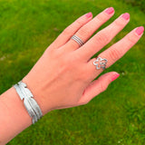 Sølvfarvet armbånd med bladdesign båret på håndleddet, stylet med ringe i sølv