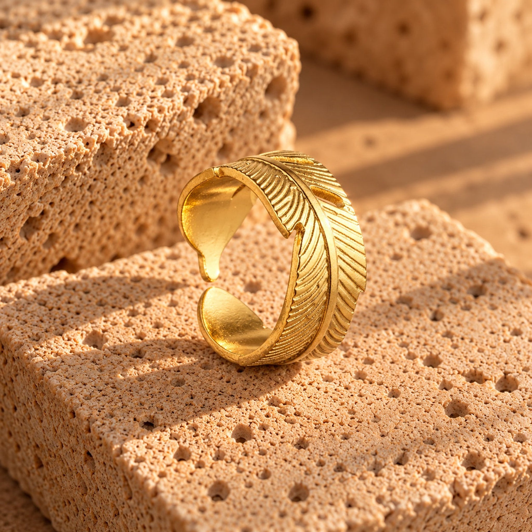 Leafy Ring i guld fra Wolff Jewelry stående på porøse sten i sollys