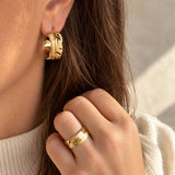 Ring i guld med blad-look båret på fingeren af model i lys strik