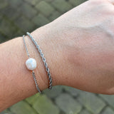 Sølvfarvet armbånd med hvid perle på håndled, stylet sammen med et snoet kædearmbånd
