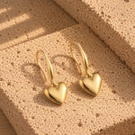 Love Heart Hoops øreringe i guld liggende på en lys, porøs sten i sollys
