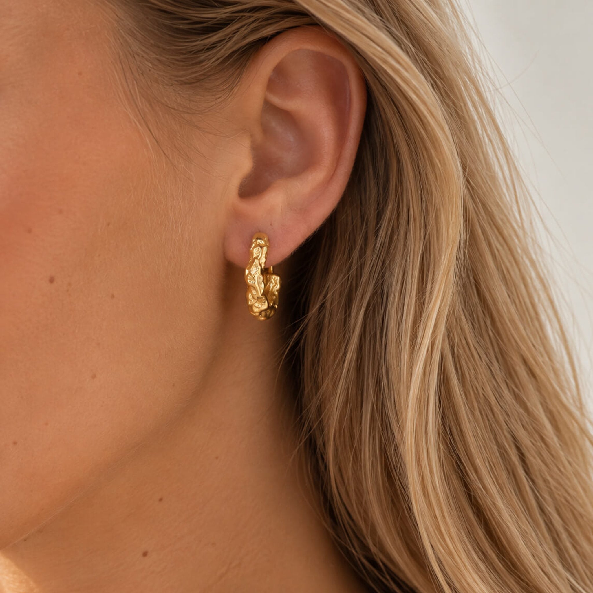 Model med lyst hår bærer Luna Big ørering i guld med struktureret overflade i øret, tæt på