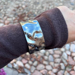 Mindy Big Bangle armbånd i sølv båret uden på ærmet af en brun strik