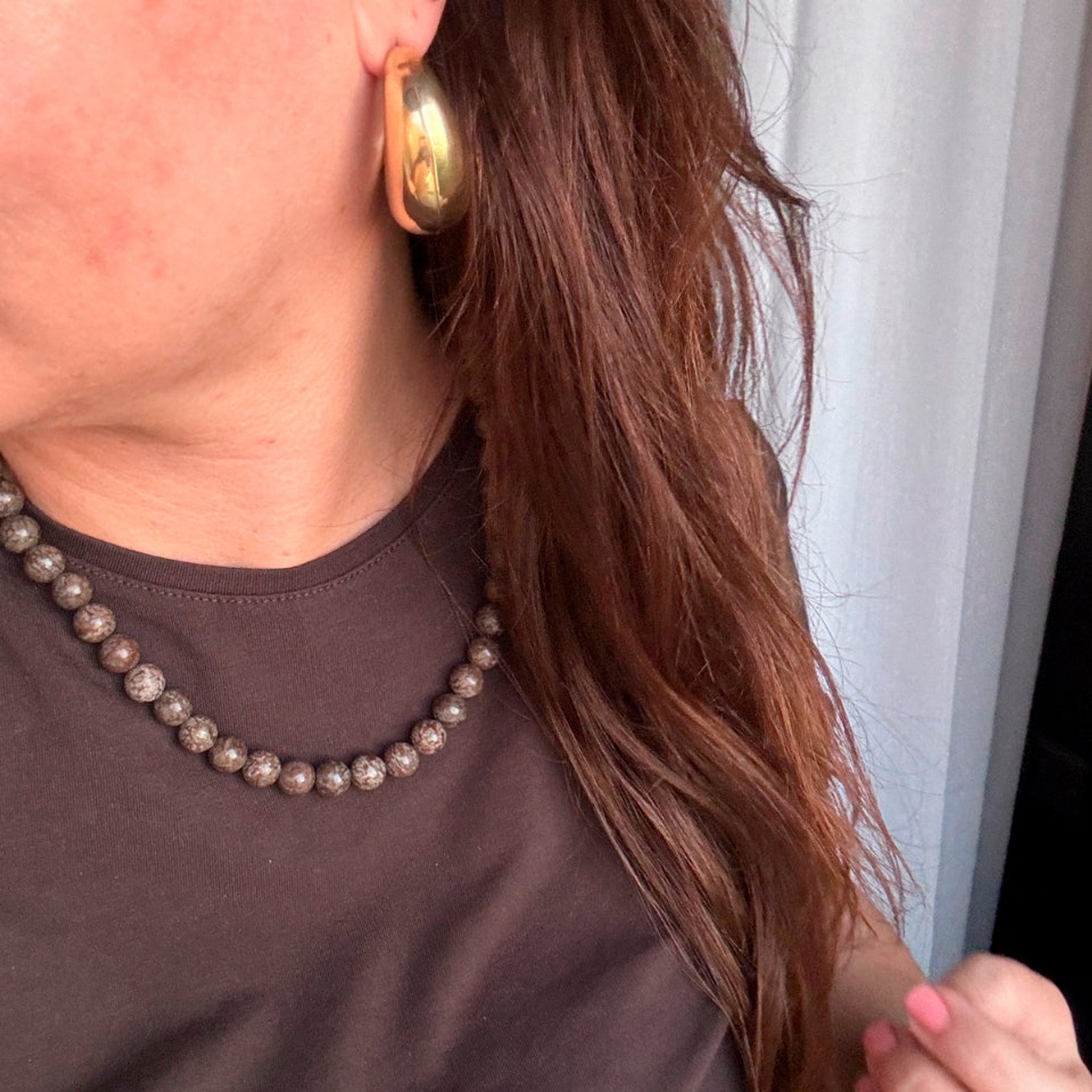 Model med guldfarvede Mindy Hoops øreringe i øret og langt brunt hår, stylet med brun t-shirt