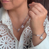 Sølvfarvet armbånd med aflange led om håndleddet, stylet med vedhæng, halskæde og hvid skjorte med blonder