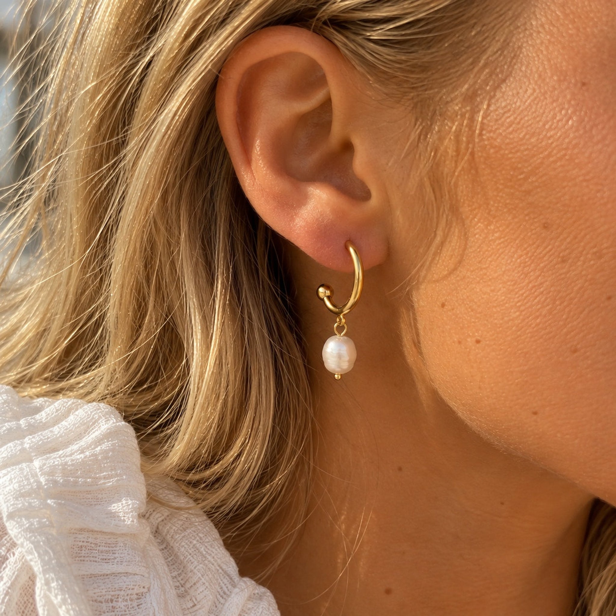 Guldfarvet ørering med hvid perle fra Wolff Jewelry båret i øret på model med lyst hår