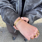 Guldfarvet Rustic Bangle armbånd på håndled, stylet med tennisarmbånd, guldringe og læderjakke