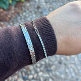 Rustic Bangle sølvfarvet armbånd båret på håndleddet over et brunt strikærme sammen med et andet armbånd