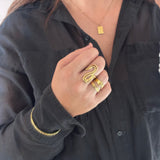 Hånd med flere guldfarvede ringe, herunder en smal hamret ring, styled med sort skjorte og halskæde