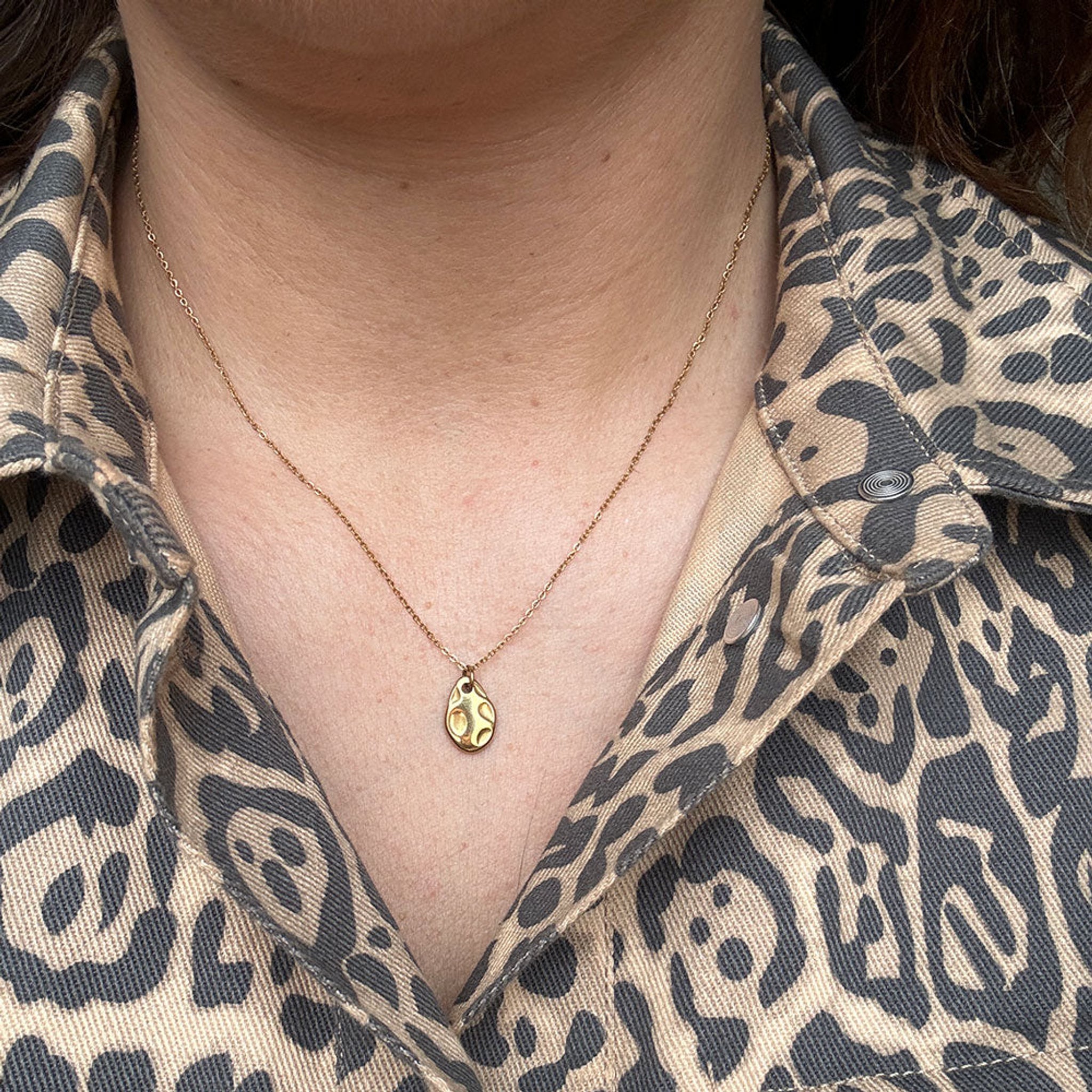 Halskæde i guld med dråbeformet vedhæng båret om halsen til en åben skjorte med leopardmønster