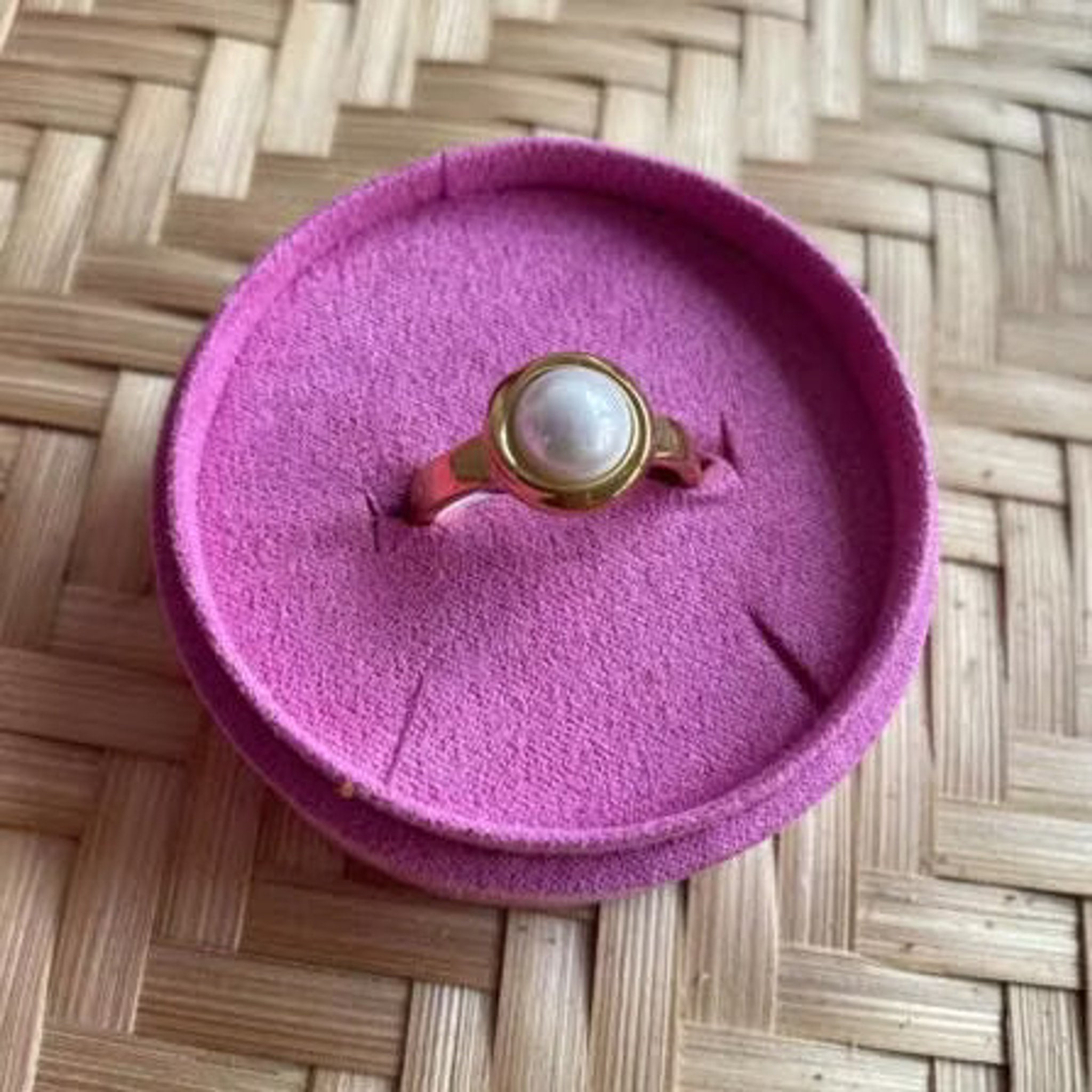Guldfarvet Sally Mini Pearl Ring med lille hvid perle i rund indfatning, placeret i en pink ringholder