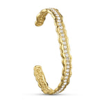 Åbent armbånd i guld med en række klare sten og bølget kant, set fra siden på lys baggrund