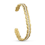 Åbent armbånd i guld med en række klare sten og bølget kant, set fra siden på lys baggrund