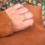 Sunny Petit Ring i guld båret på fingeren, hånd hviler på brunt ruskind