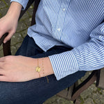 Guldfarvet armbånd med rund mønt på håndleddet, stylet med stribet skjorte og jeans