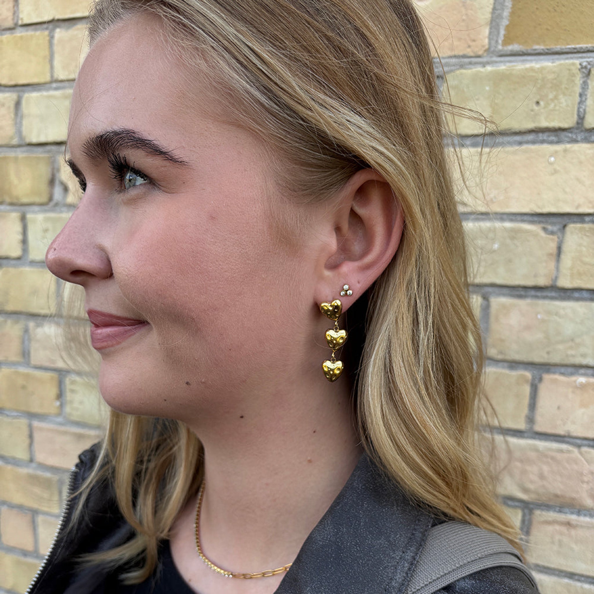 Model med Tara ørering i guld højt i øret sammen med hængeøreringe med hjerter