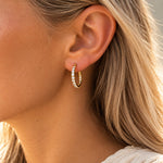 Model med lyst hår bærer Tara Hoops øreringe i guld med klare sten, set tæt på i profil