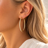 Model bærer Tara Hoops øreringe i guld med klare sten, tæt på øret