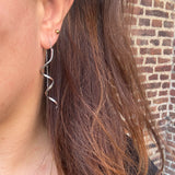 Model med brunt hår bærer sølvfarvet spiralørering med kæde fra Wolff Jewelry, set fra siden
