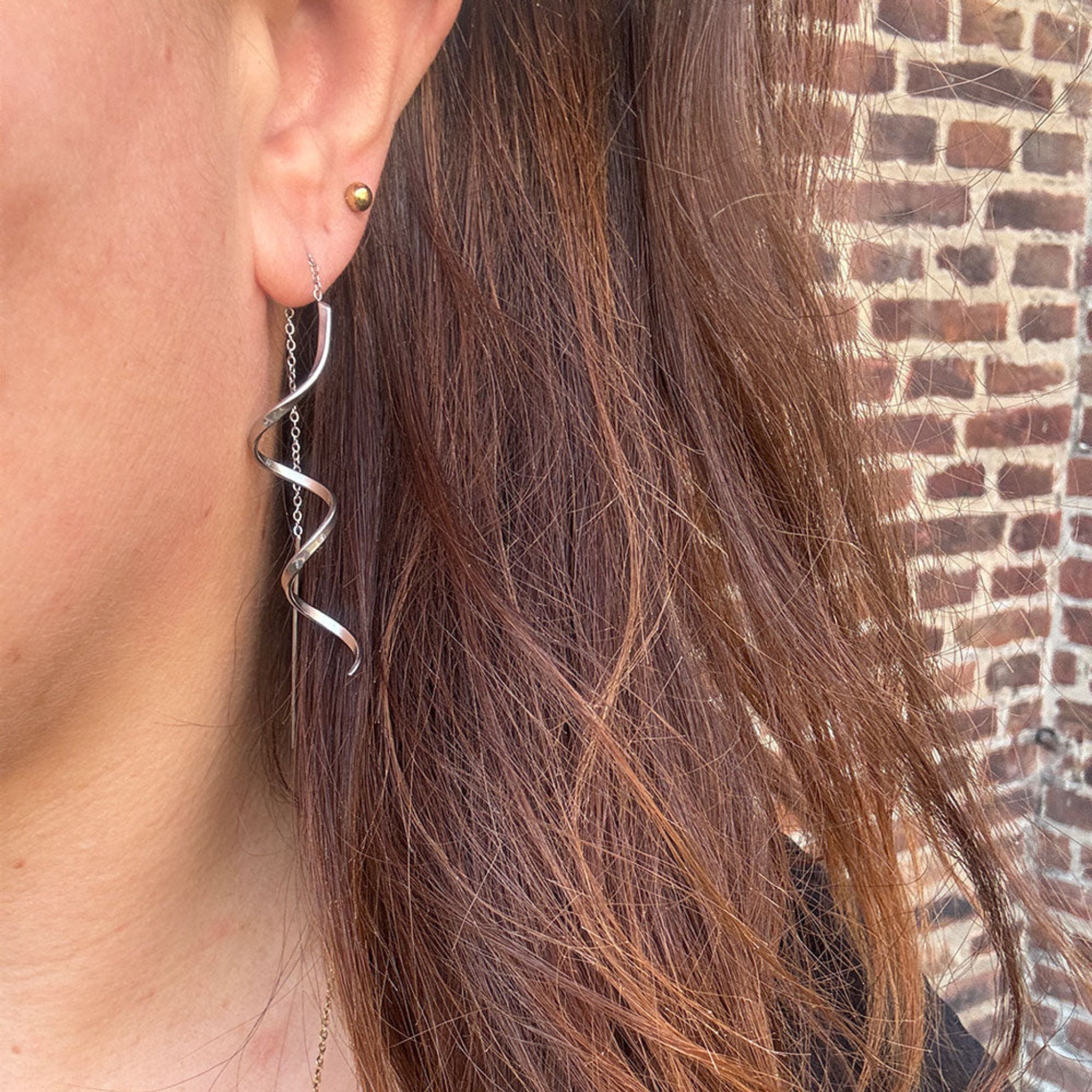 Model med brunt hår bærer sølvfarvet spiralørering med kæde fra Wolff Jewelry, set fra siden