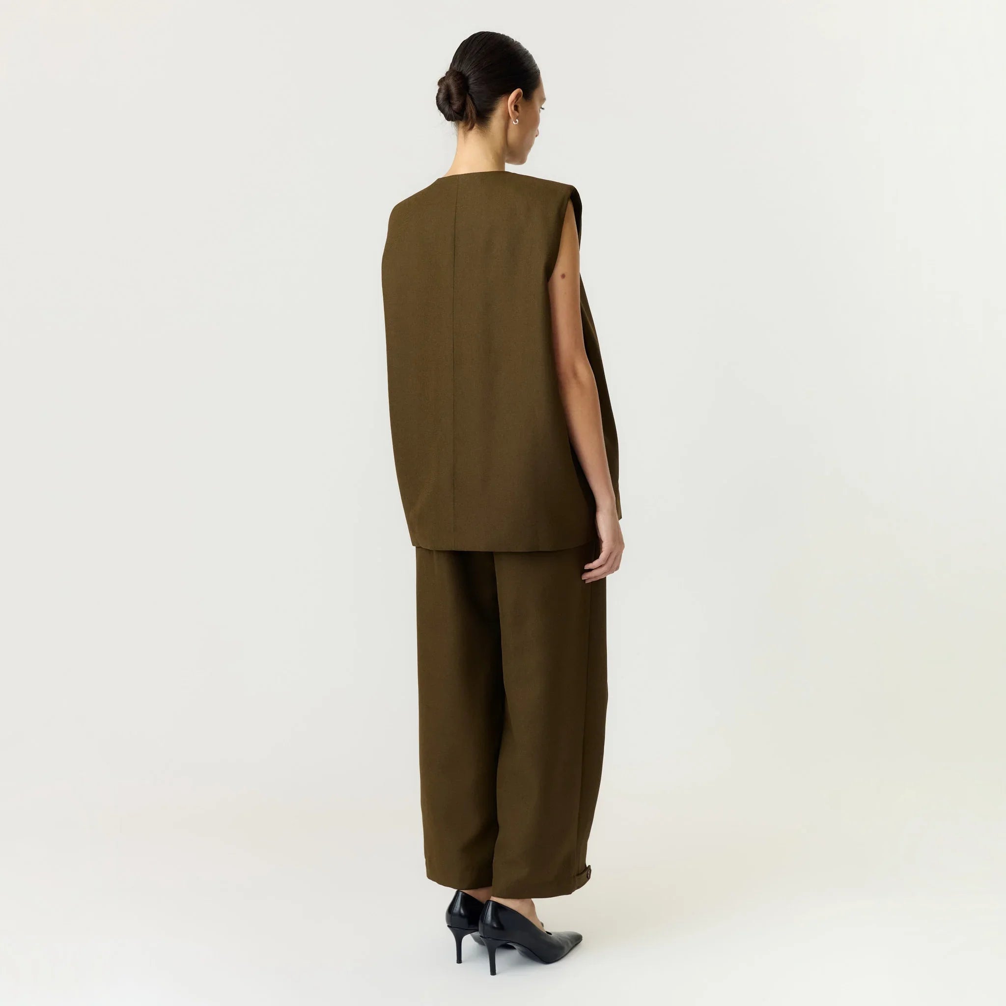 Model i grøn Yascolera vest fra YAS set bagfra, stylet med bukser i samme farve og sorte pumps