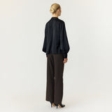 Model i sort bluse med lige kant forneden, set bagfra i hel figur